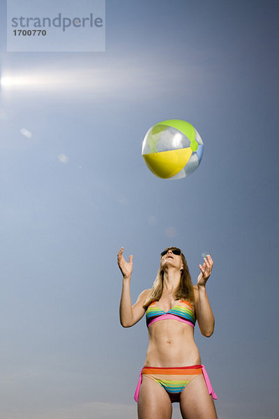 Young woman wearing bikini  throwing beach ball