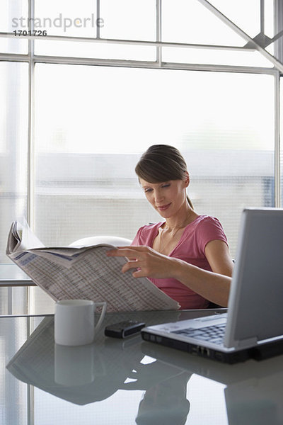 Frau am Schreibtisch liest Zeitung