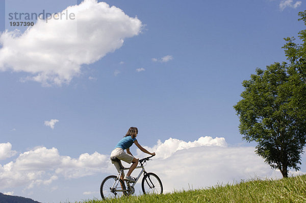 Junge Frau beim Radfahren auf der Wiese  Rückansicht