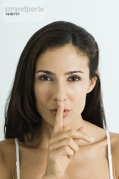 Frau hält den Finger über die Lippen  schaut in die Kamera  Porträt  Mund