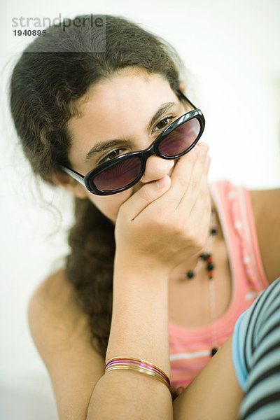 Preteen Mädchen hält Hand über Mund  schaut über Sonnenbrille  Portrait