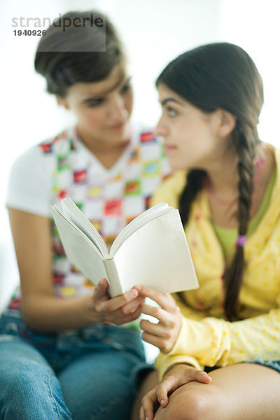 Junge Freundinnen lesen gemeinsam ein Buch und schauen sich an.