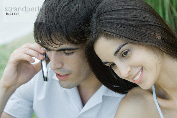 Junges Paar  Frau lehnt Kopf gegen Mann  während Mann Handy  Kopf und Schultern benutzt  Porträt