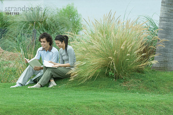 Paar auf Rasen sitzend  Bücher lesend