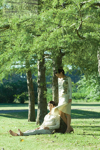 Paar unter Baum  Mann auf Gras sitzend  während Frau steht