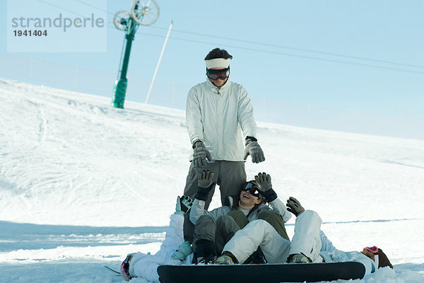 Junge Snowboarder liegen auf dem Boden und greifen nach einem jungen Mann  der hinter ihnen steht.