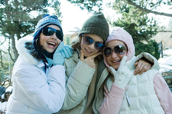 Drei Teenagermädchen in Winterkleidung und Sonnenbrille  Kinn haltend  lachend