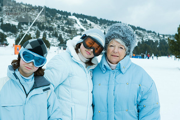 Seniorin mit Teenagern und Enkelinnen  die Mäntel und Hüte tragen und in verschneiter Landschaft stehen.