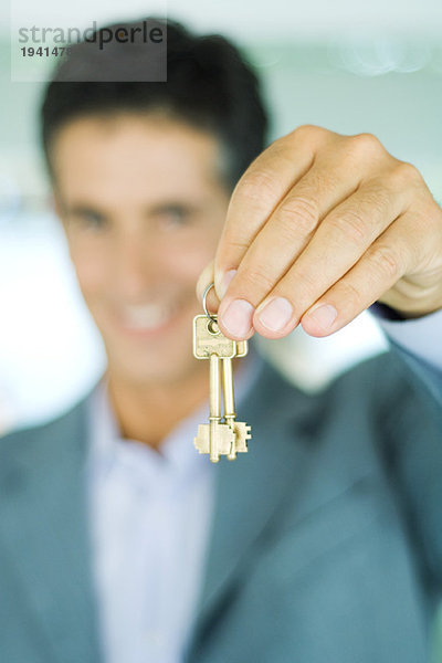 Immobilienmakler hält Schlüssel hoch  Fokus auf Schlüssel im Vordergrund  Nahaufnahme