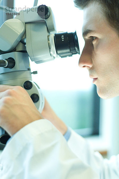 Junge männliche Wissenschaftlerin beim Blick durchs Mikroskop  Nahaufnahme