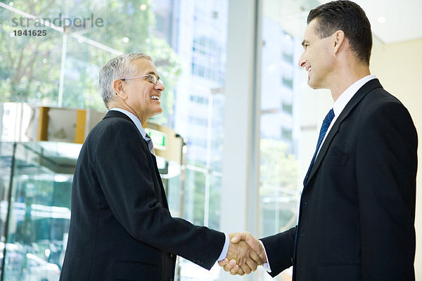 Zwei Geschäftsleute schütteln sich die Hände  lächeln sich an  taillieren sich.