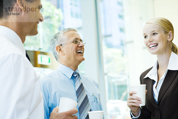 Geschäftspartner lachen gemeinsam  halten heiße Getränke in der Hand