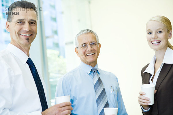 Drei Geschäftspartner lächelnd vor der Kamera  mit heißen Getränken  Portrait