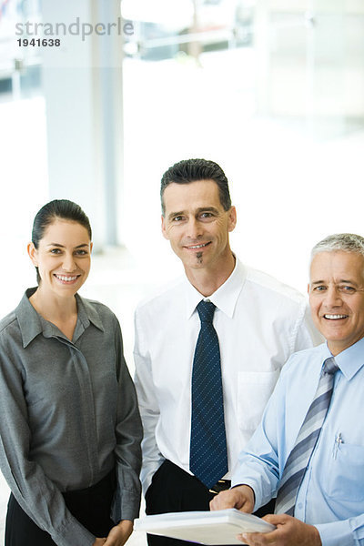 Drei Geschäftspartner stehen zusammen und lächeln in die Kamera.