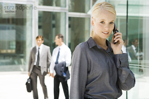 Junge Geschäftsfrau mit Handy  lächelt in die Kamera  Geschäftsleute im Hintergrund