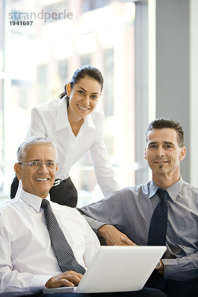 Drei Geschäftspartner lächeln vor der Kamera  Gruppenportrait  einer am Laptop