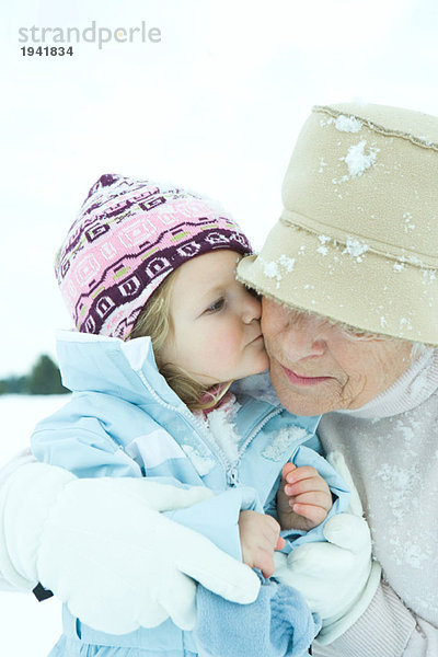 Kleinkind Mädchen küsst Großmutter auf Wange im Schnee  Nahaufnahme