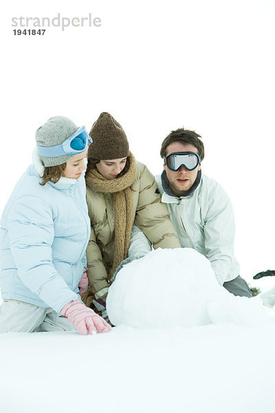 Drei junge Freunde hocken im Schnee  machen Schneeball  einer schaut in die Kamera....