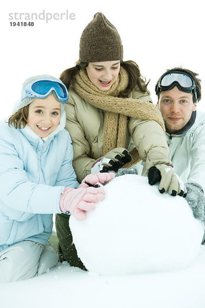 Drei junge Freunde hocken im Schnee  machen zusammen große Schneebälle  zwei lächeln vor der Kamera