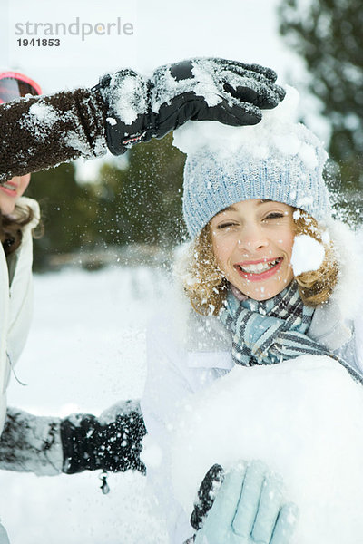 Teenagermädchen wird mit Schneebällen getroffen  lächelt in die Kamera