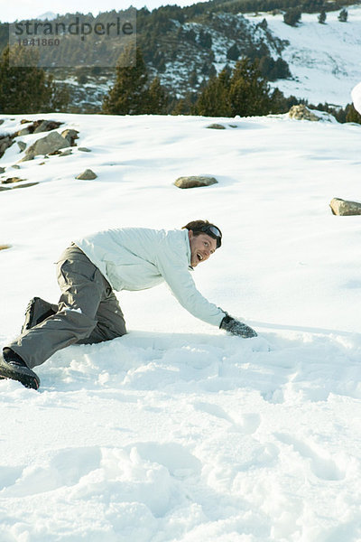 Junger Mann auf allen Vieren im Schnee  lächelnd  volle Länge