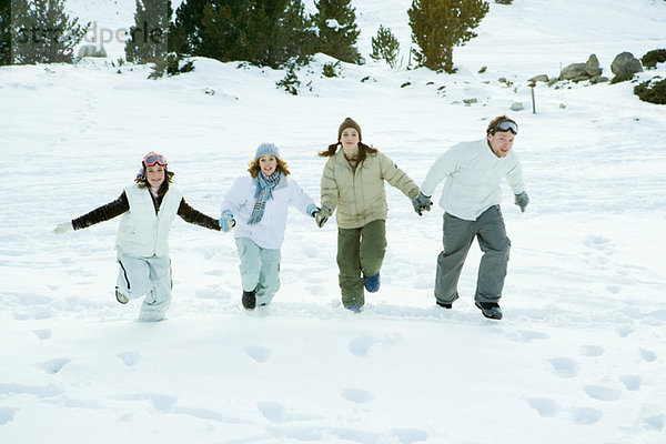 Vier junge Freunde  die zusammen im Schnee laufen  Händchen haltend  volle Länge