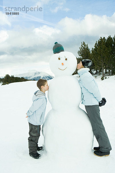 Schwester und Bruder stehend  Schneemann küssen  Seitenansicht