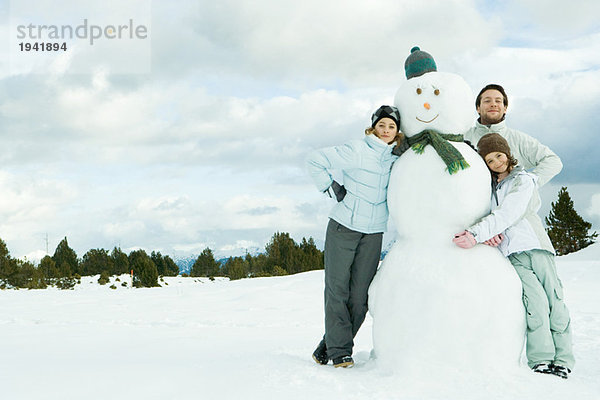 Drei junge Freunde  die sich gegen den Schneemann lehnen  lächeln vor der Kamera  Porträt