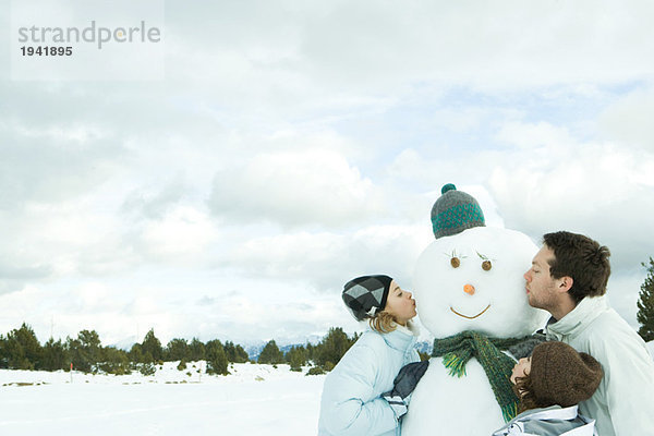 Drei junge Freunde küssen Schneemann  Kopf und Schultern