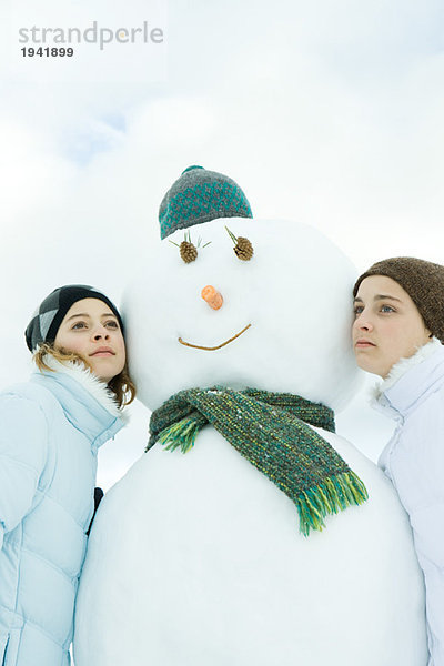 Zwei Teenager-Mädchen  die sich gegen den Schneemann lehnen  wegschauen  Porträt