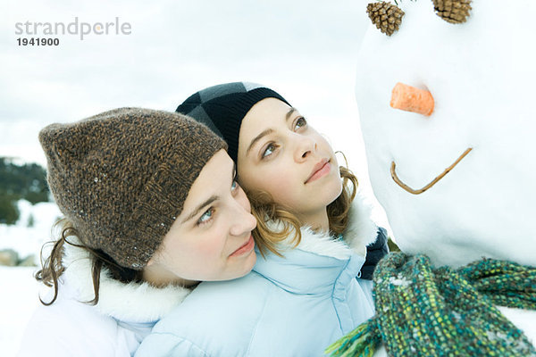 Zwei Teenager-Mädchen  die zusammen den Schneemann anschauen  der eine mit dem Kopf auf der Schulter des anderen.