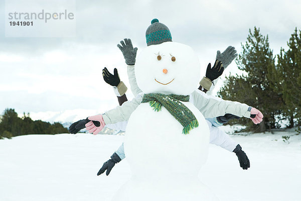 Junge Freunde verstecken sich hinter Schneemann  Arme ausstrecken