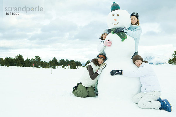 Vier junge Freunde  die den Schneemann umarmen  Gruppenporträt  einer mit Blick auf die Kamera