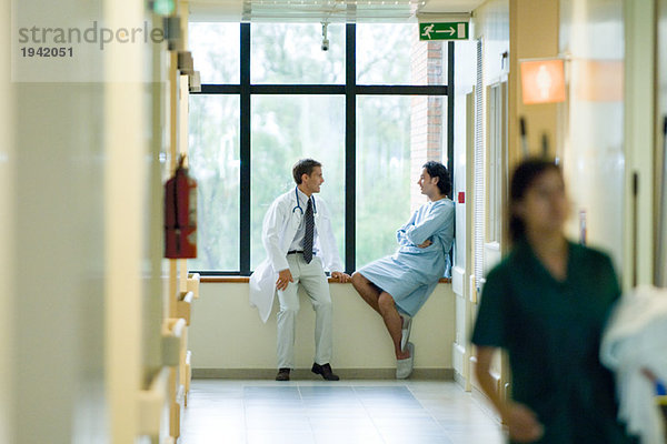 Männlicher Arzt und Patient sitzen am Fenster im Flur des Krankenhauses  diskutieren  Fokus auf Hintergrund