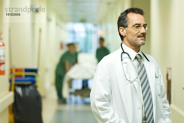 Männlicher Arzt schaut weg  lächelnd  Krankenhausflur im Hintergrund