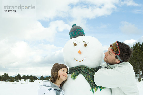 Bruder und Schwester umarmen Schneemann  lächelnd  Kopf und Schultern