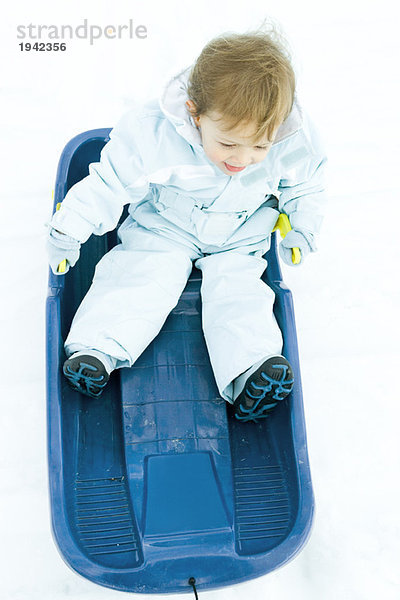 Kleinkind auf dem Schlitten sitzend  in Winterkleidung gekleidet  Blick in den hohen Winkel