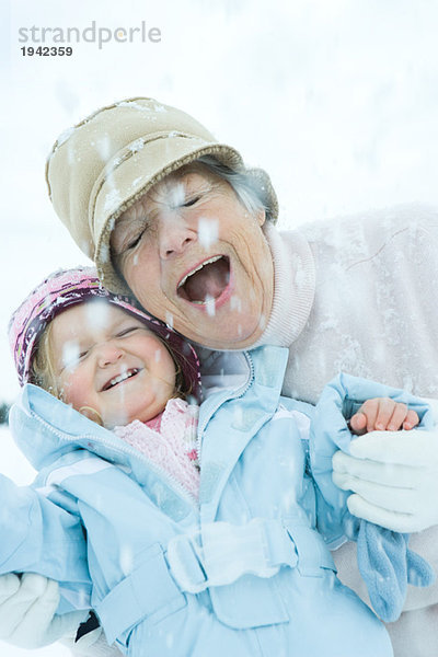 Seniorin und Enkelin Wange an Wange im Schnee  lächelnd  Augen  geschlossen