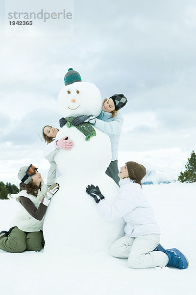 Junge Freunde umarmen Schneemann  lächelnd  volle Länge