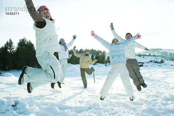 Junge Freunde  die in die Luft springen  in Winterkleidung gekleidet  lächelnd in die Kamera schauen