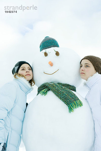 Zwei junge Freunde  die sich gegen den Schneemann lehnen  wegschauen  Porträt