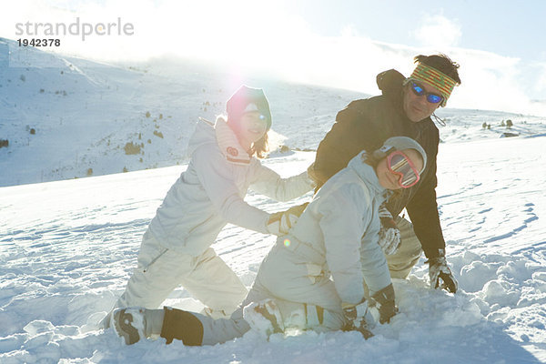 Vater und zwei Töchter kauernd im Schnee  lächelnd