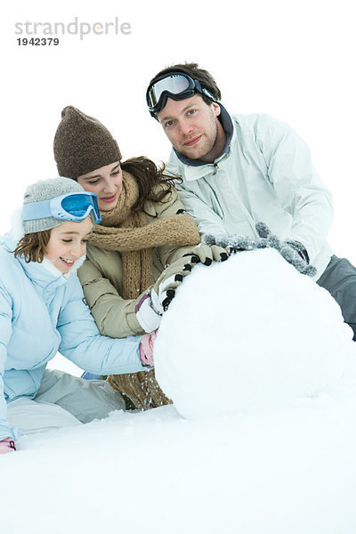 Drei junge Freunde  die Schneeball machen  gekleidet in Winterkleidung  einer mit Blick auf die Kamera