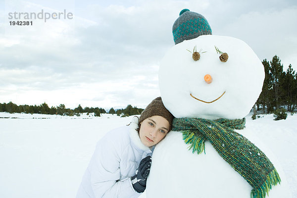 Teenagermädchen lehnt sich gegen Schneemann  schaut weg  Portrait