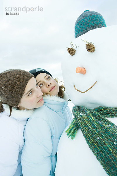 Zwei junge Freunde schauen zusammen auf den Schneemann  einer lehnt sich auf die Schulter des anderen.