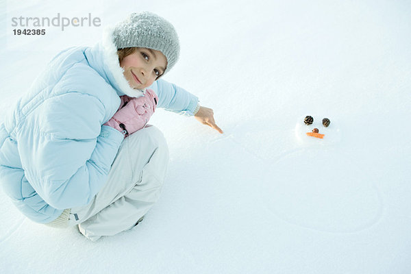 Preteen Mädchen hocken im Schnee  Zeichnung Schneemann  lächelnd in der Kamera
