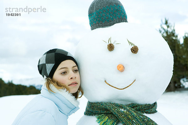 Teenagermädchen lehnt sich an Schneemann  Wange an Wange  Portrait