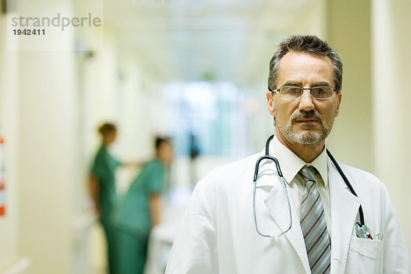 Männlicher Arzt steht im Flur des Krankenhauses und schaut auf Kamera  Kopf und Schultern.