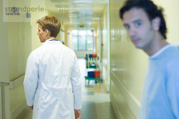 Männlicher Arzt im Krankenhausgang  Rückansicht  Mann mit Blick auf die Kamera im Vordergrund