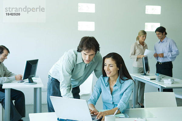 Geschäftsmann und Geschäftsfrau im Büro  mit Laptop  Mitarbeiter im Hintergrund